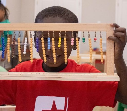A boy in a red Star Lab T-shirt peers through a wooden frame of hanging colored bead chains.