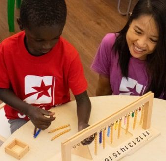 A boy in a red Star Lab T-shirt slides beads on a wooden bead-counting frame while a smiling woman in a purple T-shirt watches beside him.