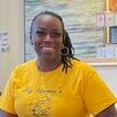 Danette Williams, smiling, in a yellow T-shirt in a classroom.