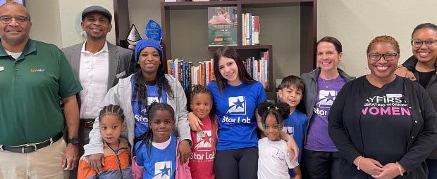 Adults and children, several wearing blue or purple Star Lab T-shirts, pose together in front of a bookshelf.