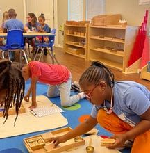 A teacher and children working with wooden Montessori materials on floor mats in a classroom.