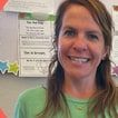 Natalia Pal, smiling, in a green T-shirt in front of a classroom wall of posters.