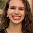 Sabina Valery, smiling, with long curly brown hair, outdoors.