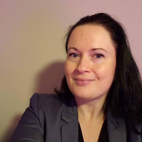 Stephanie Seketa, with long dark hair and a dark blazer, against a pink wall.