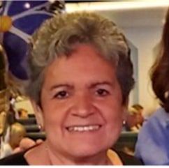 Sue Fair, smiling, with short gray curly hair, at an indoor event.